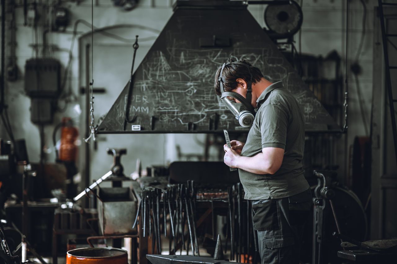 A man wearing a mask works in a metal workshop, demonstrating industrial craftsmanship.